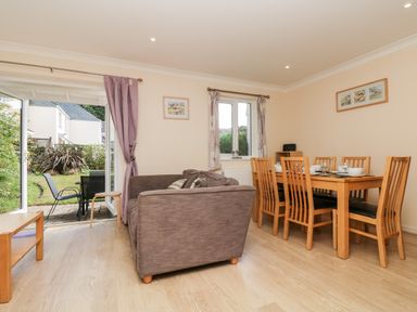 A dining area with wooden dining table and chairs next to a living area with a brown sofa and open doors to a garden at Trelease in Falmouth