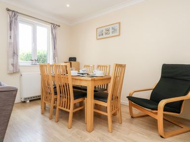 A dining area with a wooden table and six chairs near a window and a black armchair at Trelease in Falmouth