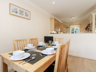 A dining area with wooden table set for six people and kitchen in the background at Trealse in Falmouth