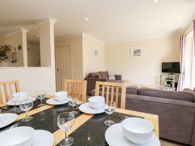 A dining table set with white bowls plates and glasses next to a living room with sofas a television and framed pictures at Trelease in Falmouth
