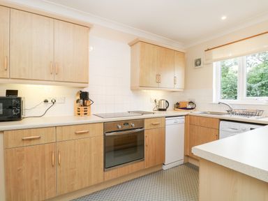 A kitchen with wooden cabinets a built in oven a dishwasher microwave and a window at Treacle in Falmouth