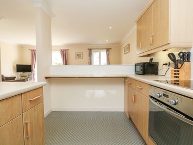A kitchen with wooden cabinets a microwave and utensils with a living room visible in the background at Trelease in Falmouth