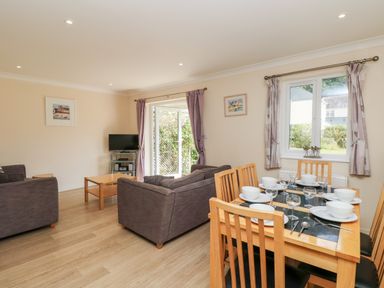 A living area with a dining table set with plates bowls and glasses a sofa a television and doors leading outside at Trelease in Falmouth