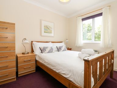 A bedroom with a wooden bed and white bedding beside a wooden dresser and nightstand at Treloose in Falmouth