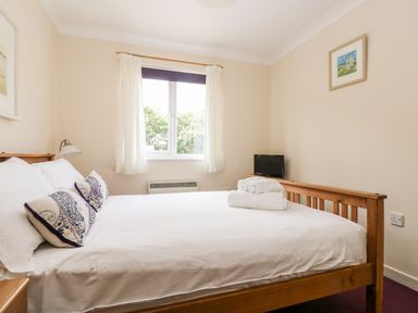 A bedroom with a wooden bed with white linens and pillows with a window and a small TV at Trellace in Falmouth