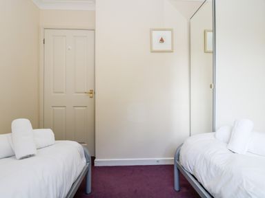 A bedroom with two single beds with white bedding and towels on each bed a door and a framed picture on the wall at Trelease in Falmouth