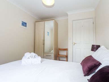 A bedroom with a bed with purple pillows and folded towels on it a wooden wardrobe with a mirror a wooden chair and a door at Trelease in Falmouth