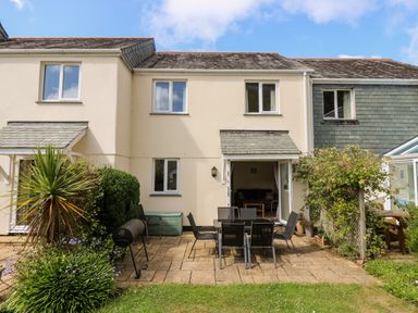 A patio with outdoor dining table and chairs outside a two-story house with an open door at Treaslece in Falmouth
