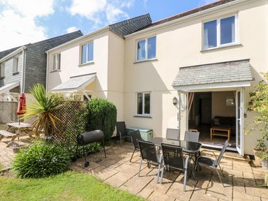 An outdoor patio with a glass table and six chairs a barbecue and plants outside a two story house at Trelease in Falmouth