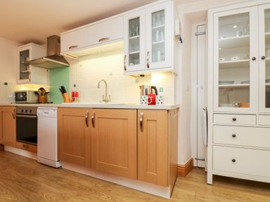 A kitchen with wooden lower cabinets white upper cabinets a stove dishwasher sink and a glass door cupboard at Plum Cottage Colebrooke near Crediton