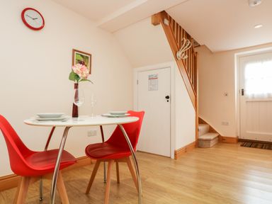 A dining area with a round white table and red chairs near stairs and a door at Plum Cottage in Colebrooke near Crediton