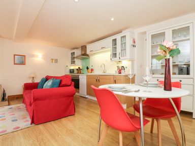A kitchen and dining area with red chairs a white table a red sofa and wooden cabinets at Plum Cottage in Colebrooke near Crediton