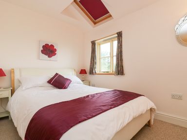 A bedroom with a double bed a skylight window a painting of a red flower and bedside tables with lamps at Plum Cottage in Colebrooke near Crediton