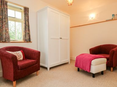 A room with two red armchairs a white wardrobe and an ottoman with a pink throw at Plum Cottage Colebrooke near Crediton