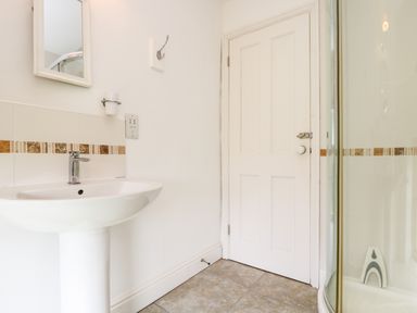 A bathroom with a pedestal sink a mirror a door and a shower enclosure at Plum Cottage in Colebrooke near Crediton