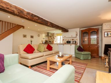 A living room with sofas and a wooden coffee table near an open kitchen with white cabinets at Apple Cottage in Colebrooke near Crediton