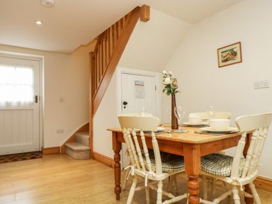 A dining area with a wooden table set for four with chairs under stairs and a door at Apple Cottage Colebrooke near Crediton