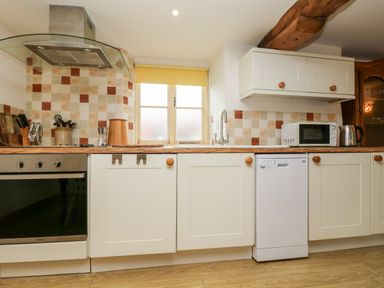 A kitchen with white cabinets wooden countertop tiled backsplash and appliances at Apple Cottage in Colebrooke near Crediton