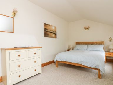 A bedroom with a wooden bed and blue bedding a cream chest of drawers and wall art at Apple Cottage in Colebrooke near Crediton