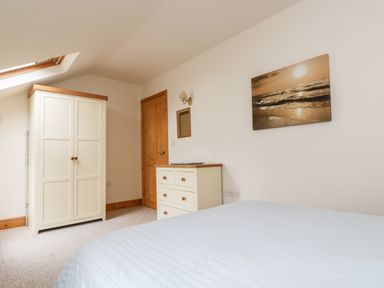 A bedroom with a white wardrobe a chest of drawers a wooden door and a bed at Apple Cottage in Colebrooke near Crediton