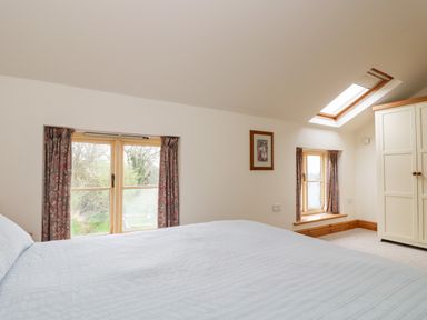 A bedroom with a bed near two windows a skylight and a wardrobe at Apple Cottage in Colebrooke near Crediton