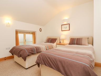 A bedroom with two single beds a nightstand lamp and a window with curtains at Apple Cottage Colebrooke near Crediton