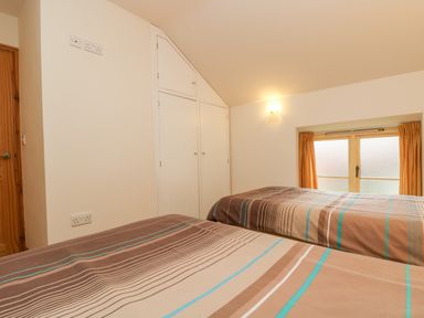 A bedroom with two single beds with striped bedding built in cupboards a wooden door and a small window with curtains at Apple Cottage in Colebrooke near Crediton