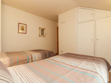 A bedroom with two single beds striped bedspreads white built in wardrobes a framed picture and a mirror on the wall at Apple Cottage in Colebrooke near Crediton