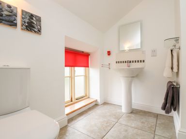 A bathroom with a toilet sink mirror red window blind and towels at Apple Cottage in Colebrooke near Crediton