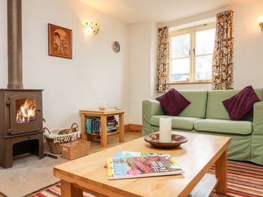 A living room with a wood-burning stove sofa with purple cushions wooden tables and a window at Apple Cottage Colebrooke near Crediton