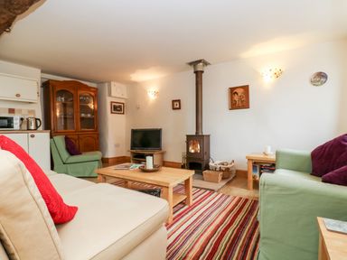 A living room with a wood burning stove a television a wooden cabinet sofa and armchairs at Apple Cottage in Colebrooke near Crediton