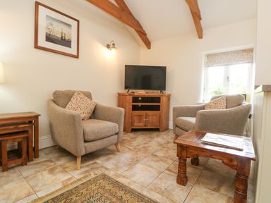 A sitting area with two armchairs a wooden TV stand with a television a wooden side table and a framed picture on the wall at Roosters in Lostwithiel