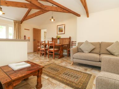 A living room with a dining table wooden chairs a beige sofa and a wooden coffee table at Roosters in Lostwithiel