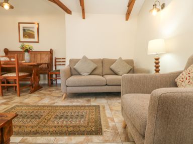 A living room with beige sofas a patterned rug a wooden dining table and chairs at Roosters in Lostwithiel
