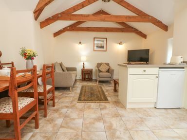 A living room with wooden chairs a dining table a sofa and armchair a TV and kitchen counter at Roosters in Lostwithiel