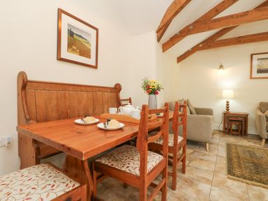 A dining area with a wooden bench and chairs around a table set with teapot and scones and a living space with armchairs and lamps at Roosters in Lostwithiel