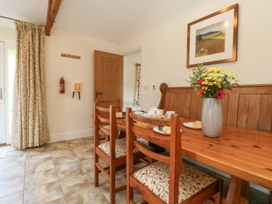 A dining area with wooden table and chairs a vase with flowers and a framed picture on the wall at Roosters in Lostwithiel