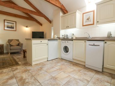 A kitchen area with appliances and a sitting area with a chair and a television at Roosters in Lostwithiel