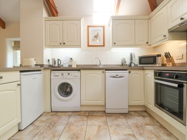 A kitchen with white cabinets appliances including washing machine dishwasher microwave oven and small fridge at Roosters in Lostwithiel
