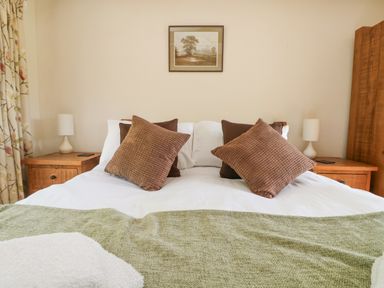 A bedroom with a double bed with brown cushions and a green blanket with wooden bedside tables and lamps at Roosters in Lostwithiel