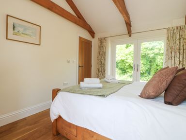 A bedroom with wooden bed frame white bedding folded towels on bed and glass doors with curtains at Roosters in Lostwithiel
