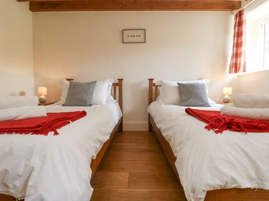 A bedroom with two single beds with red blankets and gray pillows at Roosters in Lostwithiel