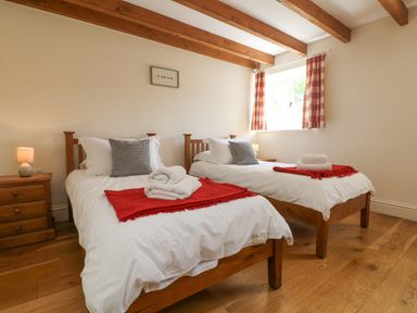 A bedroom with two single beds wooden furniture and a window with checkered curtains at Roosters in Lostwithiel