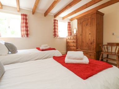 A bedroom with two single beds towels on beds wooden wardrobe chest of drawers and chair at Roosters in Lostwithiel