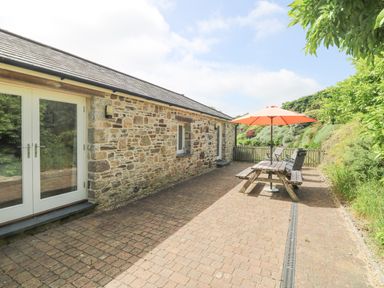 An outdoor patio area with a stone wall building wooden picnic table orange umbrella chairs and greenery at Roosters in Lostwithiel
