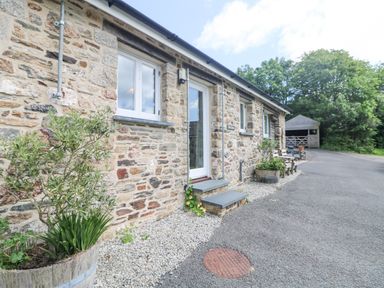 An exterior view of a stone building with white doors and windows gravel and asphalt ground with plants in wooden barrels at Byre Lostwithiel