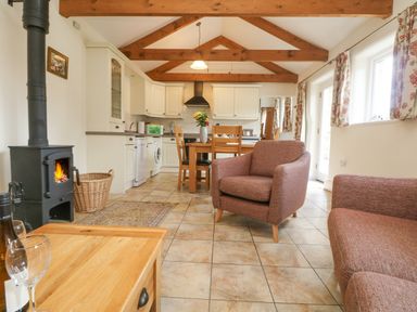 A kitchen and dining area with wooden beams on the ceiling and armchairs near a wood stove at Byre Lostwithiel