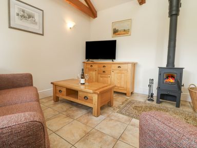 A living room with a wood stove and wooden furniture including a coffee table and sideboard at Byre in Lostwithiel
