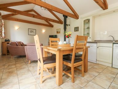A dining area with wooden table and chairs adjacent to a kitchen with white cabinets and appliances at Byre in Lostwithiel