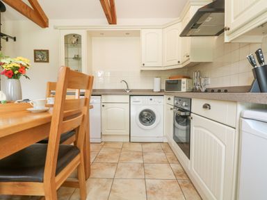 A kitchen with wooden dining table and chairs washing machine oven microwave and knives at Byre in Lostwithiel